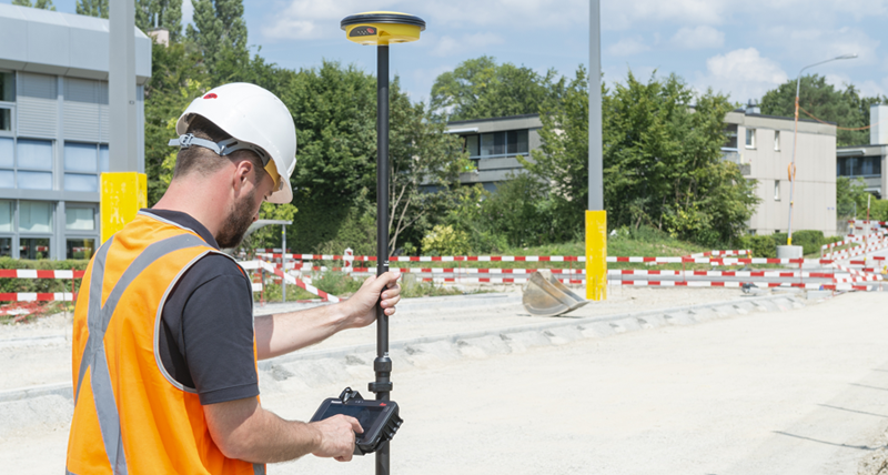 Construction worker in orange safety vest and helmet measures points with a Leica iCON CC70 field controller and a Leica iCON GPS 30.